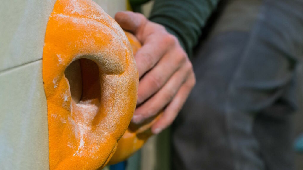 Bouldern: Kraft, Technik und Köpfchen an der Kletterwand 2 Im Bild sieht man eine Hand, die beim Bouldern nach einem Bouldergriff greift.