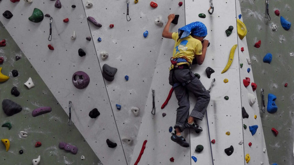 Bouldern: Kraft, Technik und Köpfchen an der Kletterwand 1 Das Bild zeigt eine Boulderhalle mit Boulderwand und einen jungen Menschen, der die Wand hochklettert.