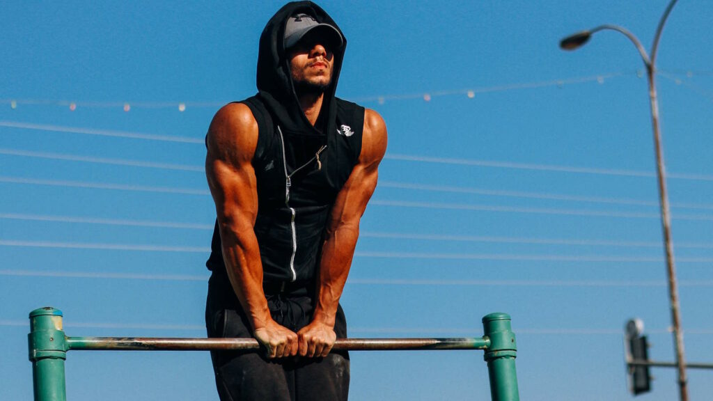 Calisthenics: Workout, Übungen, Muskelaufbau & Tipps 1 Auf dem Bild ist ein junger Mann zu sehen, der ein Calisthenics Outdoor Workout an einer Reckstange im Freien absolviert.