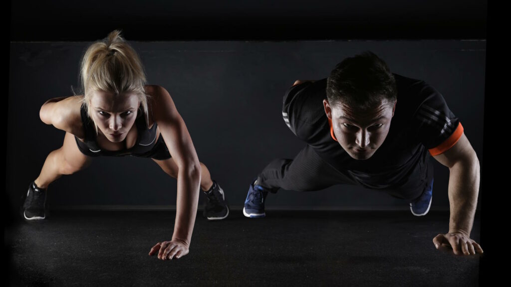 Calisthenics: Workout, Übungen, Muskelaufbau & Tipps 2 Das Bild zeigt eine weibliche und einen männlichen Athleten, die ein Calisthenics Workoaut auf dem Boden absolvieren.