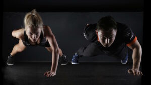 Calisthenics: Workout, Übungen, Muskelaufbau & Tipps 1 Das Bild zeigt eine weibliche und einen männlichen Athleten, die ein Calisthenics Workoaut auf dem Boden absolvieren.