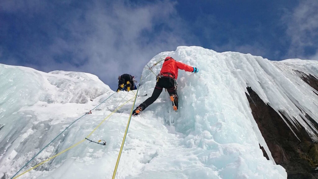 Eisklettern: Technik, Ausrüstung, Eisverhältnisse und Sicherheit an Eisfällen 3 Im Bild sieht man zwei Eiskletterer, die an einem kleinen Felsvorsprung an Eiszapfen hochklettern.