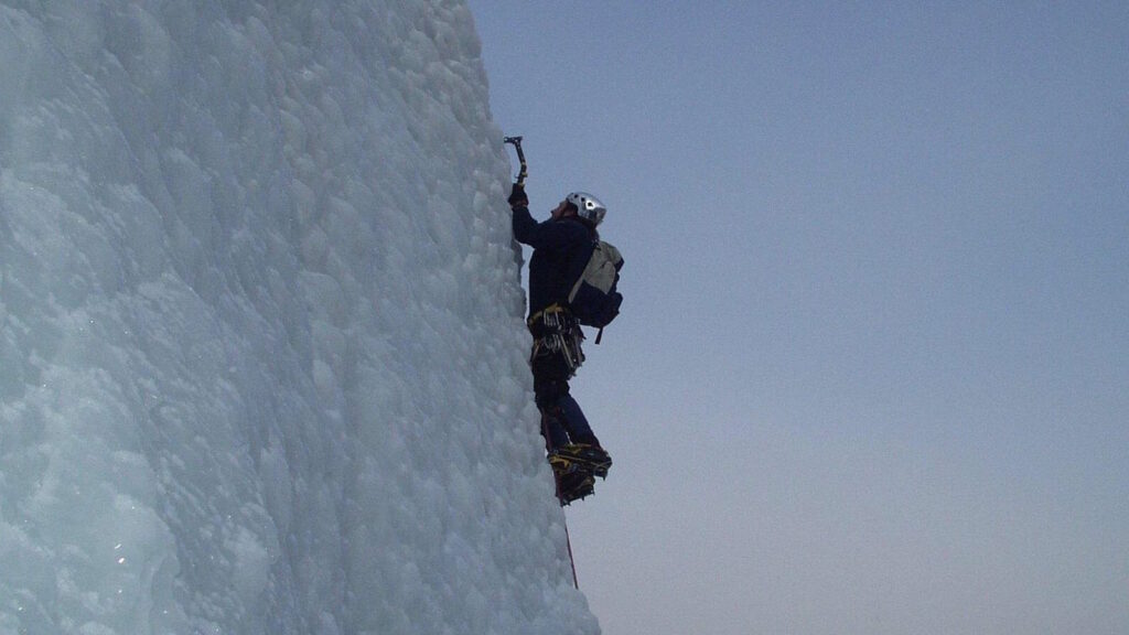Eisklettern: Technik, Ausrüstung, Eisverhältnisse und Sicherheit an Eisfällen 2 Im Bild sieht man einen Eiskletterer, der mit seiner Ausrüstung einen steilen Hang erklimmt.
