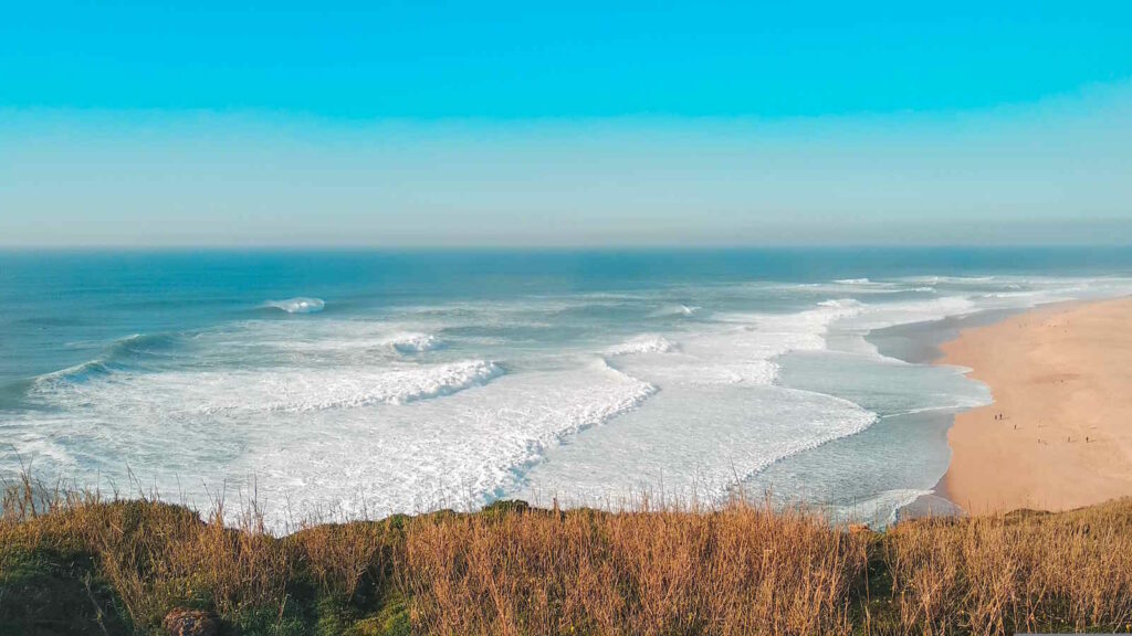 Big Wave Surfing: Große Wellen, Extremsport und die Wissenschaft hinter dem Big Wave Surfen 2 Das Bild zeigt aus der Vogelperspektive einen Strand auf Nazaré mit großen Wellen.