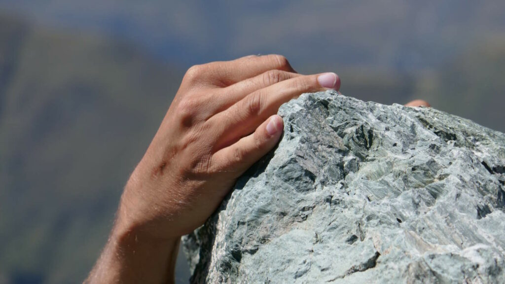 Bouldern: Kraft, Technik und Köpfchen an der Kletterwand 3 Im Bild sieht man eine Hand, die beim Outdoor-Bouldern nach einem Felsabsatz greift