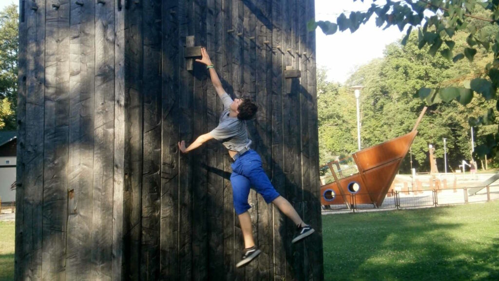 Parkour: Mehr als Springen und Klettern – die Kunst, Hindernisse zu überwinden 2 Im Bild sieht man einen jungen Mann, der die Trendsportart Parkour ausübt und dabei ein einer Mauer hochklettert.