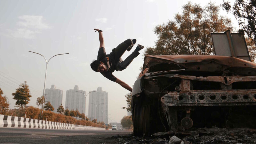 Parkour: Mehr als Springen und Klettern – die Kunst, Hindernisse zu überwinden 1 Im Bild sieht man einen jungen Mann, der auf seinem Parkour über ein verrostetes Auto springt.