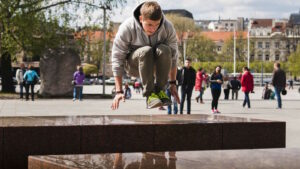 Parkour: Mehr als Springen und Klettern – die Kunst, Hindernisse zu überwinden 1 Das Bild zeigt einen jungen Mann der beim Parkour in gehockter Stellung über eine Mauer als Hindernis springt.