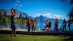 Slacklining: 10 Tipps, Vorteile & Arten erklärt 1 Das Bild zeigt eine Gruppe beim Slacklining im Park an einem See. Ein Mann balanciert auf einer Lowline, andere Personen schauen ihm dabei zu.