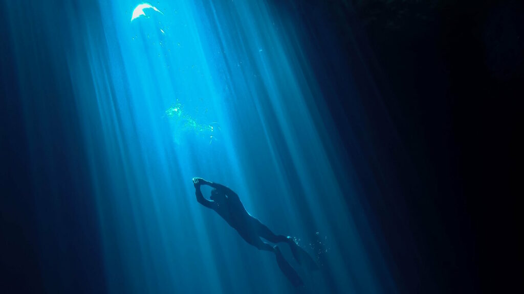 Höhlentauchen entdecken: Guide für Ausbildung, Ausrüstung, Sicherheit und faszinierende Unterwasserwelten 2 Das Bild zeigt einen Taucher beim Cave Diving, der von oben von Sonnentrahlen angestrahlt wird, die durch das Wasser in die Tiefe dringen.