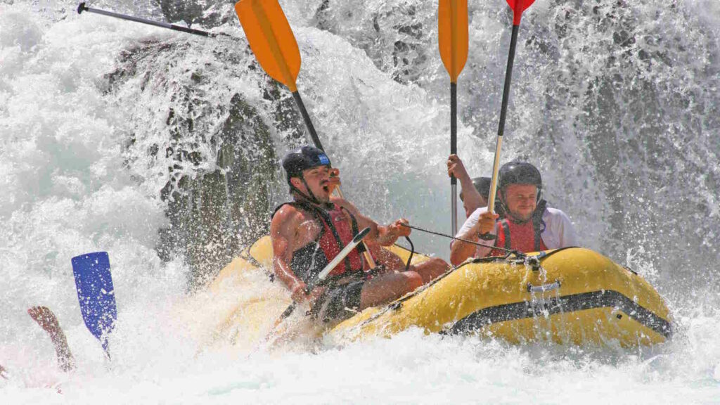 Rafting: Wildwasser-Abenteuer, Sicherheit, Schwierigkeitsgrade und praktische Tipps 2 Im Bild sieht man eine Gruppe beim Wildwasser Rafting. Es zeigt anschaulich, wie die Gicht spritzt und dass es für die Besatzung anstrengend ist.