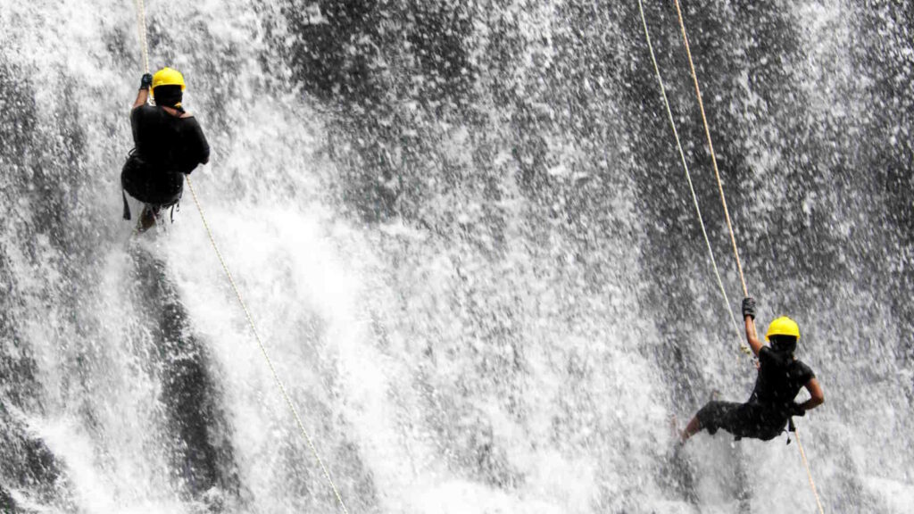 Canyoning: Die besten Tipps für ein sicheres Abenteuer 2 Das Bild zeigt zwei Personen, die sich bei einer Canyoning Tour an einer Felswand im Wasserfall abseilen.