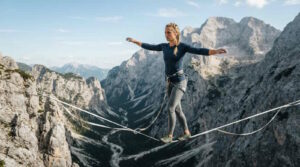 Das Bild zeigt eine Frau beim Highlining über einer Schlucht in den Alpen.