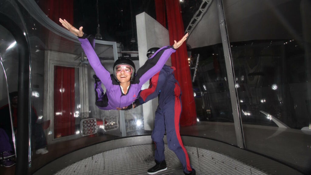 Indoor Skydiving – Bodyflying: Fliegen im Windkanal 3 Frau fliegt mit Unterstützung eines Coaches im Windkanal
